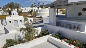 A white building with a dome and arched windows, surrounded by greenery and a clear sky. - atlantis villa - sea paradise (Santorini)
