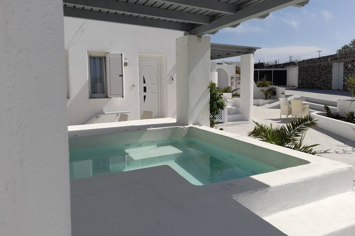 A white building with a swimming pool, outdoor seating, and a stone wall.