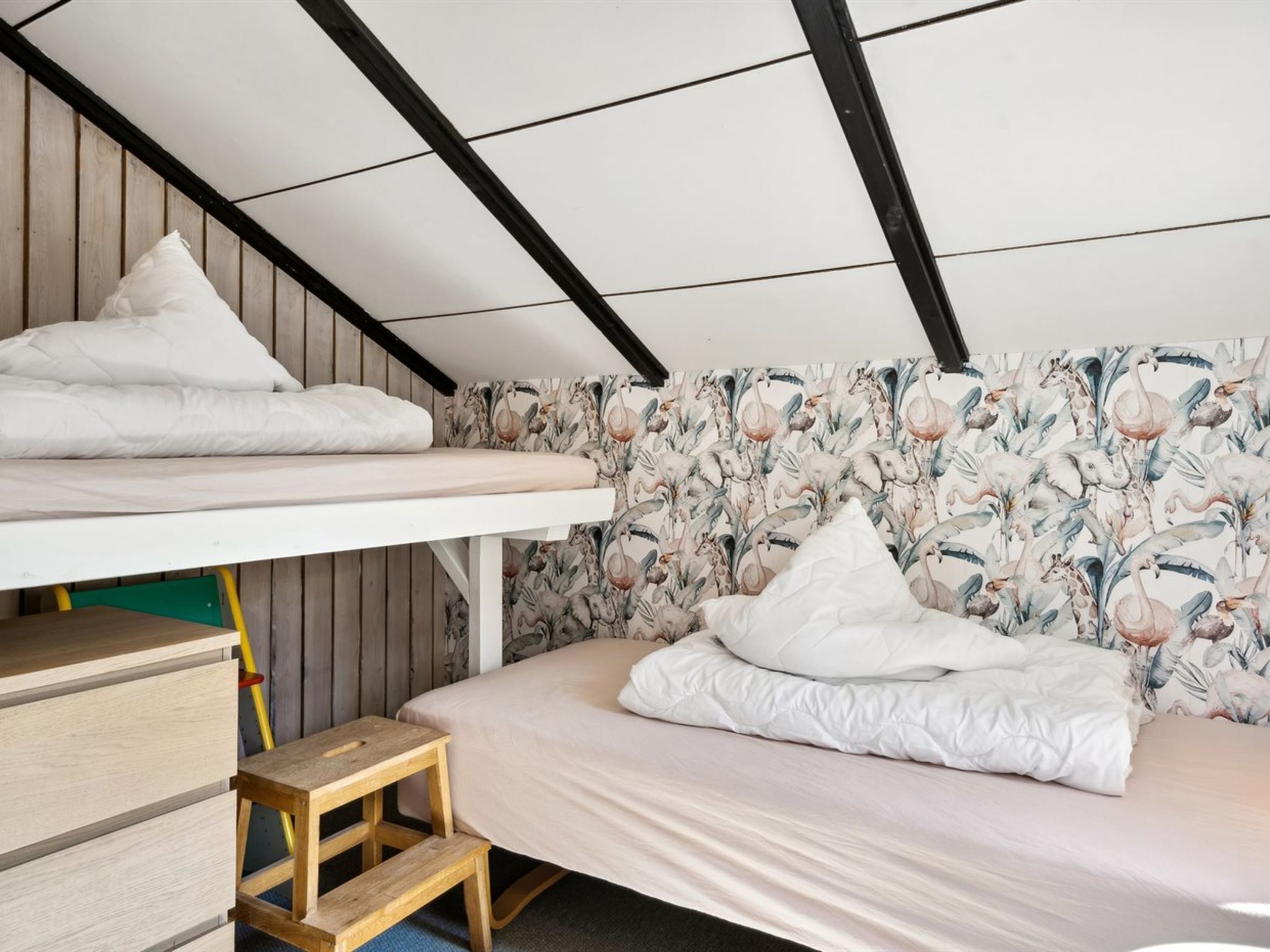 Una camera del dormitorio con un letto a castello, uno sgabello di legno e carta da parati a motivi floreali.