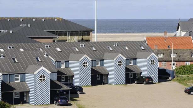 Een kusthotel met meerdere blauw-gestreepte gebouwen, uitzicht op het strand en een parkeerplaats met auto's.