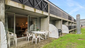 Een gebouw met een overdekt terras, inclusief een tafel en stoelen, en een grote ventilator.