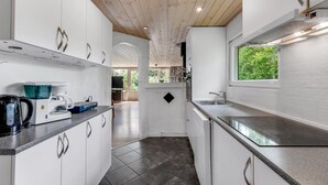A modern kitchen with white cabinets, a coffee machine, and a window providing a view of greenery outside.