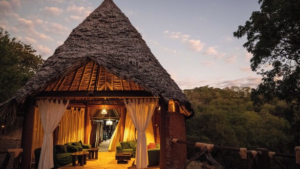 A thatched-roof hut with a covered seating area and a stone pathway leading to it.