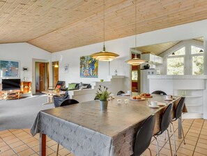 A spacious living area with a dining table, chairs, a TV, and artwork on the walls.