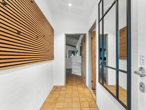 A hallway with a tiled floor, a wooden slatted wall, and a glass door with a metal handle.