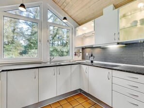 A modern kitchen with white cabinets, a black countertop, and a view of trees through large windows.