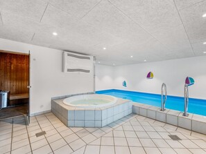A modern indoor pool area with a hot tub, a sauna, and a wooden door.