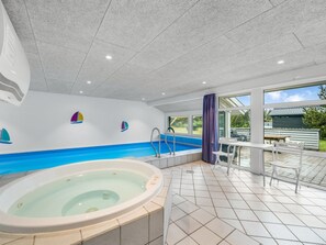 Un espace spa comprenant un bain à remous, une piscine et un coin salon couvert avec vue sur l’extérieur.
