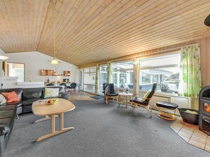A spacious living area with a wooden ceiling, a fireplace, and large windows.