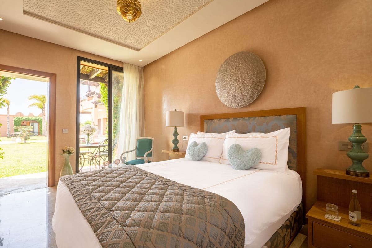 Ein Hotelzimmer mit einem großen Bett, zwei Nachttischlampen, einem Wandbild und Blick auf den Garten.