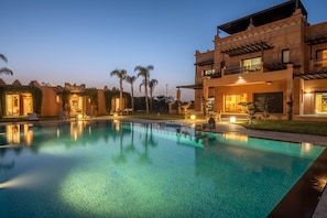 Uma piscina com espreguiçadeiras, um edifício com varandas e palmeiras.