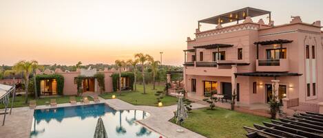 A large, modern hotel with a swimming pool, outdoor seating, and a well-maintained garden.