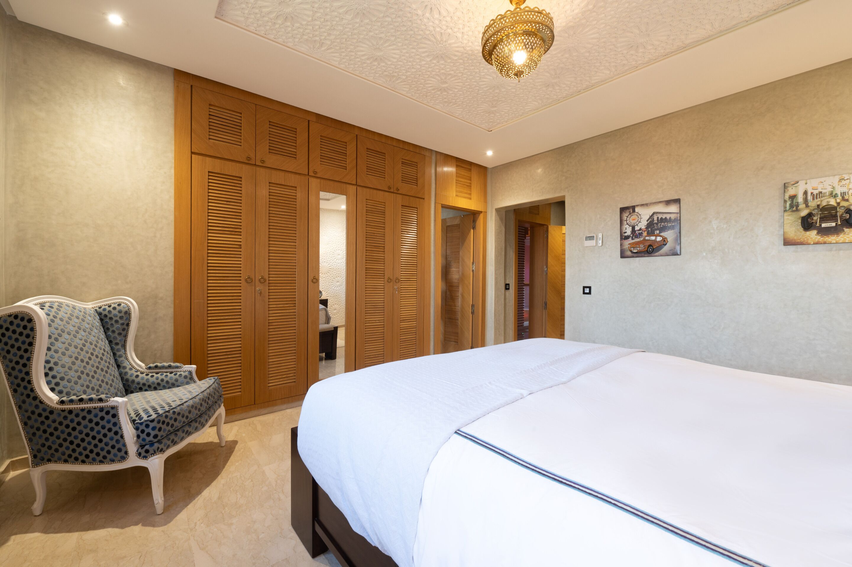 A bedroom with a large bed, wooden wardrobe, and a patterned armchair.