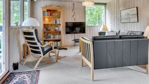Ein gemütliches Wohnzimmer mit Bücherregal, einer schwarzen Ledersofa, einem Holzstuhl, einem Fernseher und einer Chandelier.