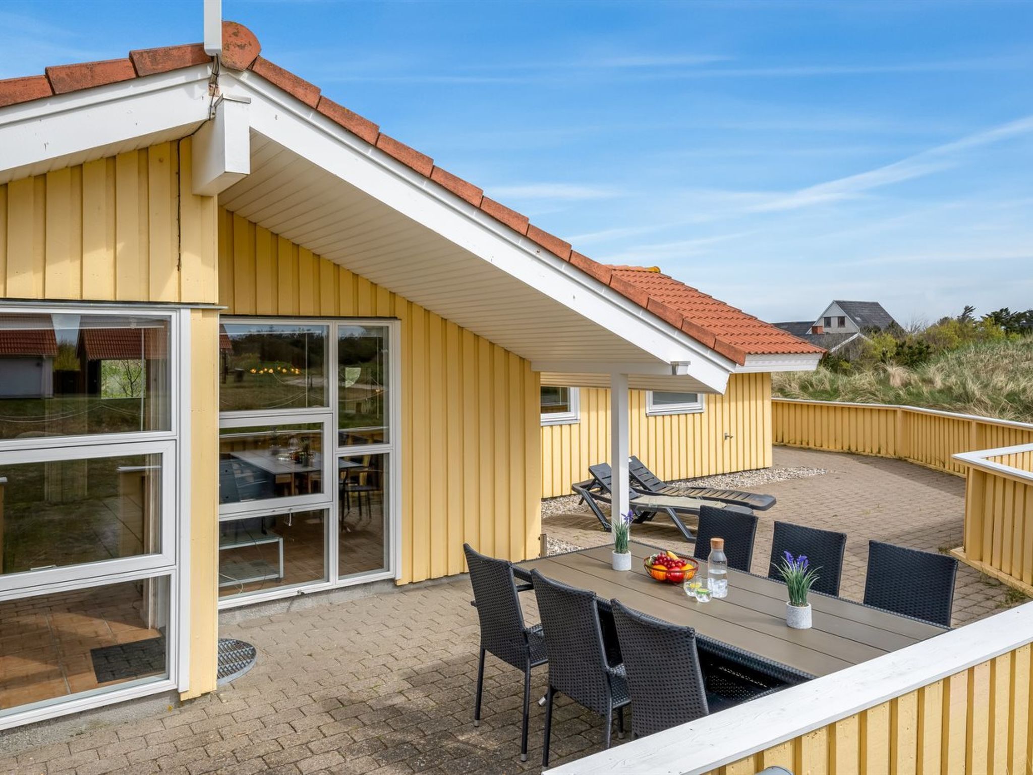 Een geel gebouw met een overdekte patio, voorzien van een tafel en stoelen, en uitzicht op het omliggende landschap.