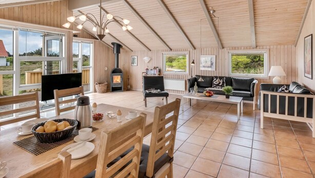 A spacious living area with a high ceiling, wooden walls, a fireplace, and a dining area with a table set for two. - "Skev" - 200m to the fjord by Interhome (Hvide Sande)