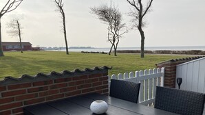 An outdoor patio with a table and chairs, a white fence, and a view of the sea.
