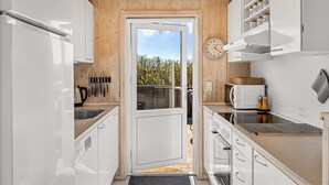 A compact kitchen with white cabinetry, a microwave, a kettle, and a clock on the wall.