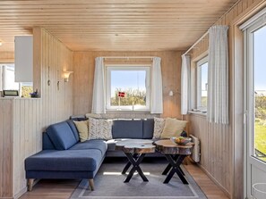 Un interior de cabaña acogedor con un sofá azul, una mesita de madera y una ventana con una bandera.