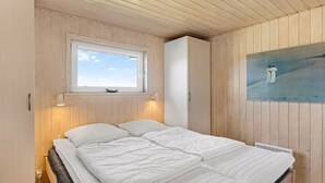 A bedroom with a bed, a window, a wall-mounted painting, and wooden paneling.
