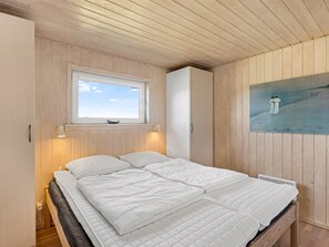 Un dormitorio con una cama, una ventana, un cuadro colgado en la pared y paneles de madera.