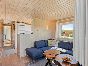 A modern interior with a wooden ceiling, a sofa, a dining table with fruit, and a window with a view.