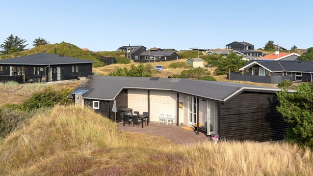 A modern house with a garage, a patio with outdoor furniture, and a view of other houses in the background. - "Jules" - 300m from the sea by Interhome (Fanø)
