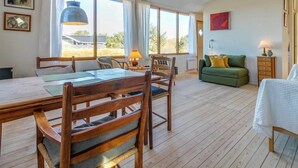 A spacious room with a wooden dining table, chairs, a sofa, and a bed. There are large windows providing natural light and a view of the outdoors. - "Jules" - 300m from the sea by Interhome (Fanø)
