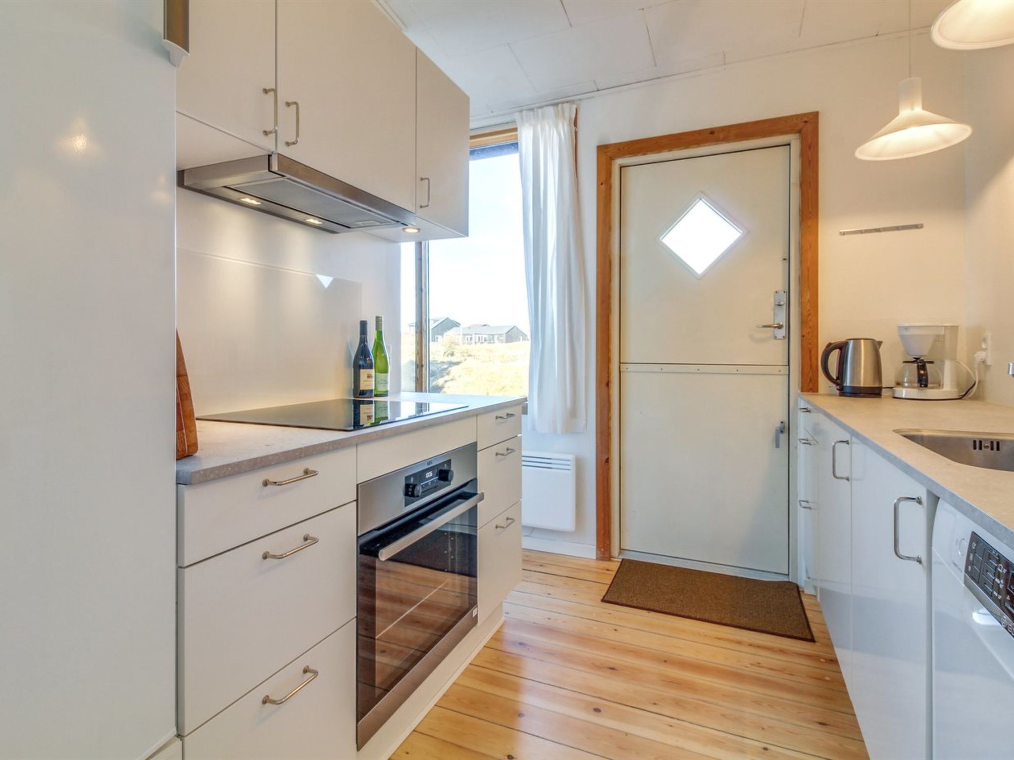 A modern kitchen with white cabinets, a built-in oven, a coffee maker, and a view through a window.