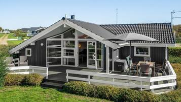 Une maison moderne dotée d’une grande terrasse, d’un espace salon extérieur abrité et offrant une vue sur le paysage environnant.