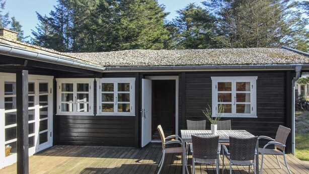 A wooden deck with a table and chairs, a covered patio area, and a dark-colored building with white-framed windows.