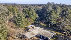 A cabin with a covered deck, a small outdoor seating area, and a view of a forested area.