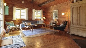 A cozy cabin interior with wooden walls and a high ceiling. There is a sofa, a chair, a table, and a cabinet.