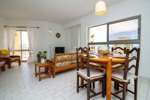 Relax in this open-plan living area with a dining set and seating arrangements, featuring a large window with a view of the surrounding buildings.