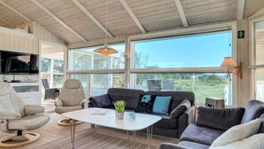 A modern living room with a large TV, comfortable seating, and a view through large windows.