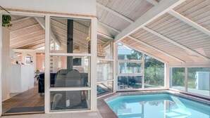 An indoor swimming pool with a view of the outdoors, a barbecue grill, and a kitchen area.