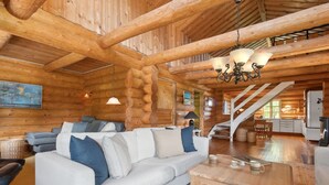 A log cabin interior with a white sofa, a wooden coffee table, a chandelier, and a staircase leading to a kitchen area. - "Elsia" - 1.5km to the fjord by Interhome (Frøstrup)