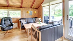 Ein gemütliches Blockhaus-Interieur mit Holzbalkendecke, einer Couch, einem Esstisch und einem Stuhl.