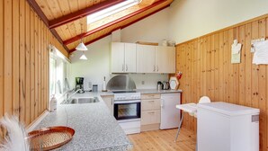 Eine kompakte Küche mit Holzwänden, einer Granitabdeckung und Grundausstattung, darunter ein Herd, ein Backofen und ein Kühlschrank.