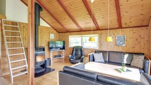 Ein gemütliches Blockhaus-Interieur mit Holzbalkendecke, Kamin, einer Couch, einem Fernseher und einer Leiter.
