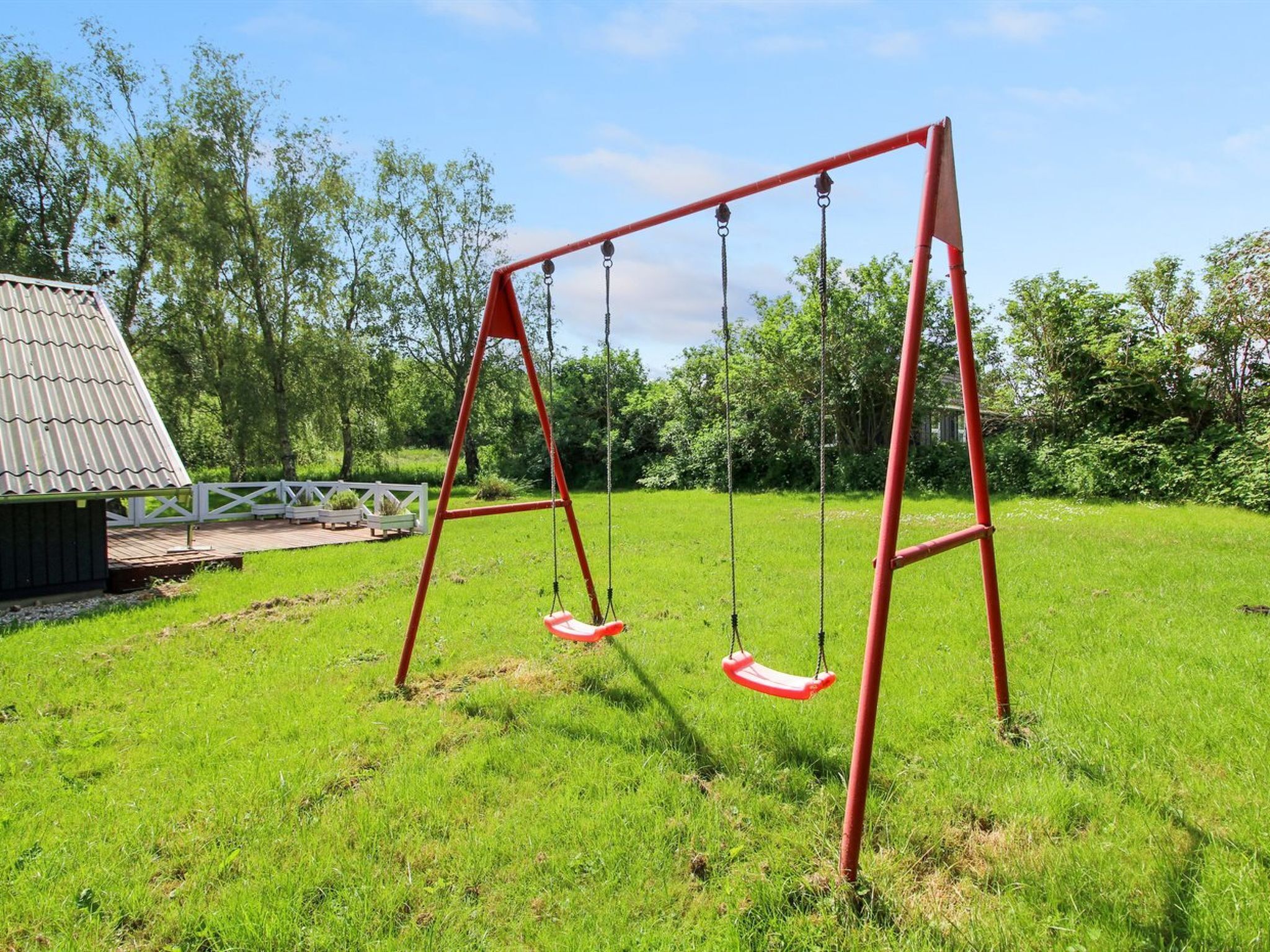 A swing set in a grassy area with a wooden structure in the background.
