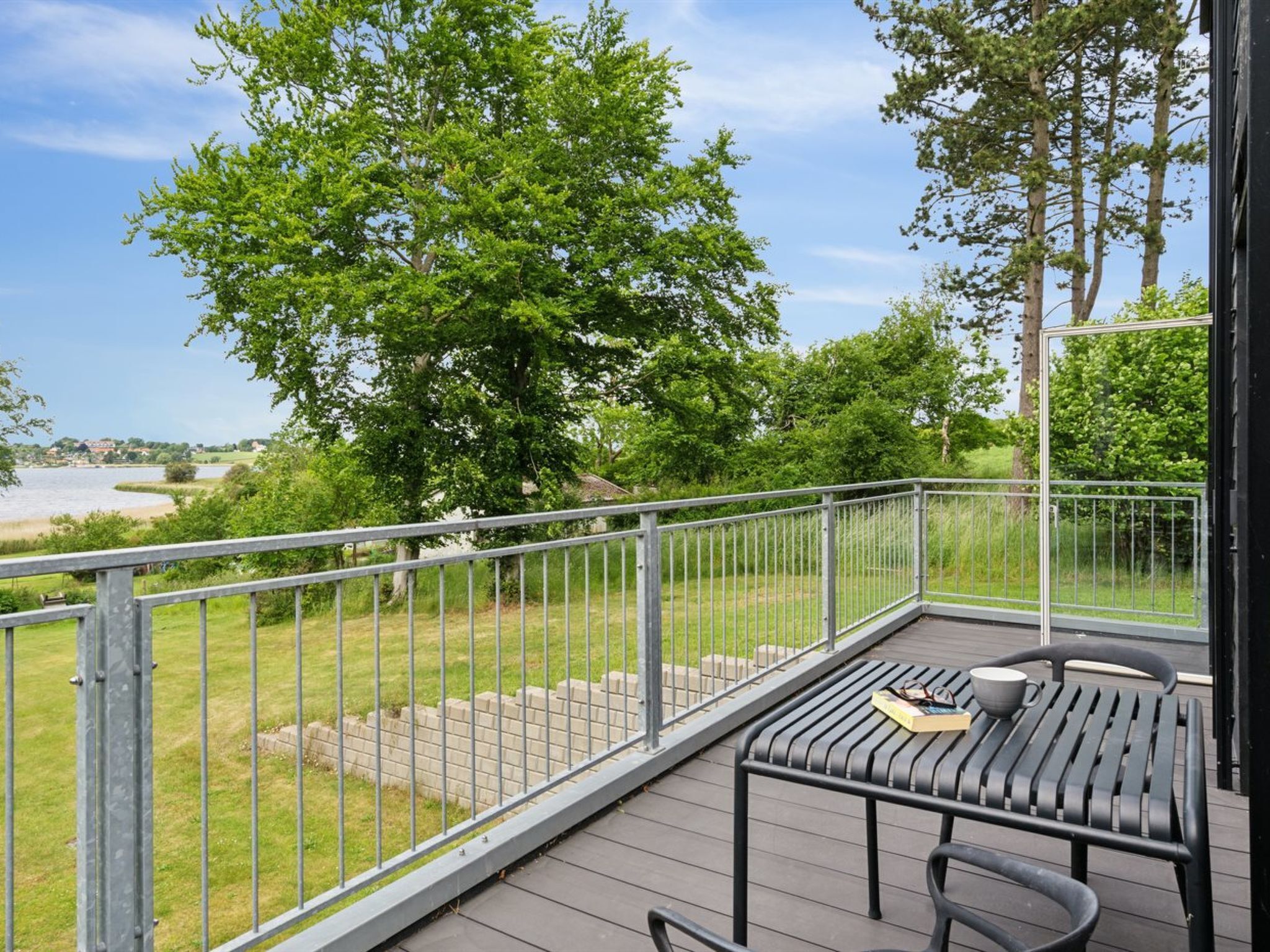 A deck with a table and chairs, overlooking a grassy area and a body of water.