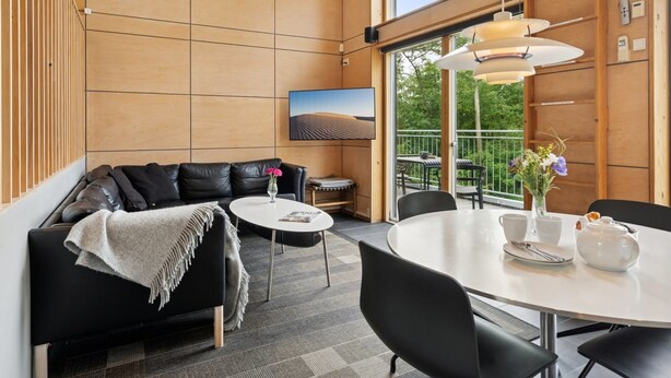 A modern interior with a black leather sofa, a round dining table, and a balcony with outdoor seating. - "Harka" - 100m to the fjord by Interhome (Roskilde)
