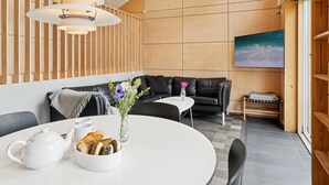 A modern interior with a wooden slat wall, a black leather sofa, a round white table with a teapot and pastries, and a painting on the wall. - "Harka" - 100m to the fjord by Interhome (Roskilde)