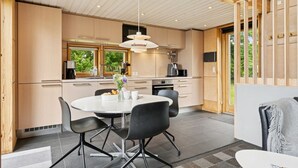 A modern kitchen with wooden beams, a dining area with a round table and chairs, and a view of greenery outside. - "Harka" - 100m to the fjord by Interhome (Roskilde)