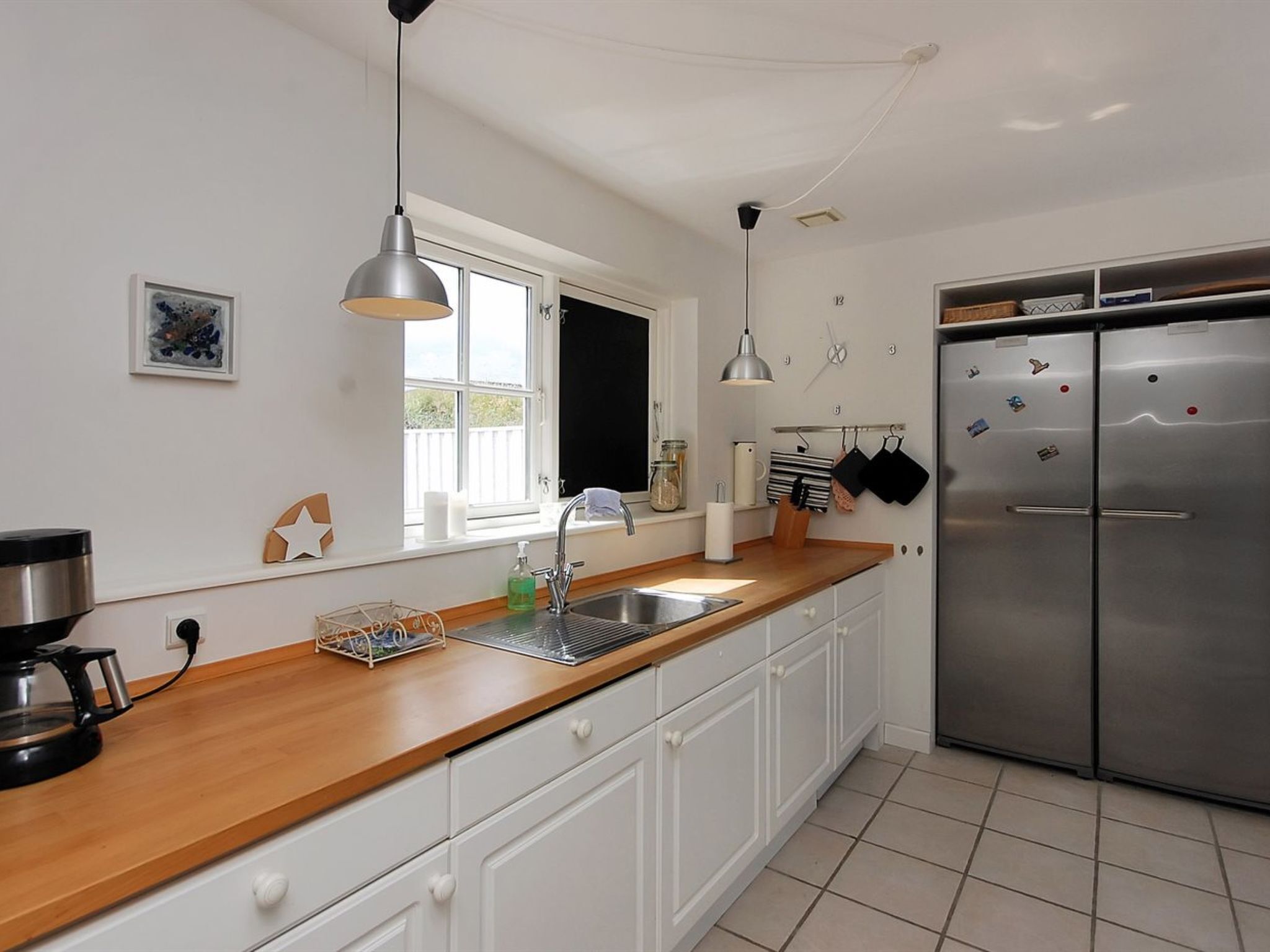 Una cocina moderna con armarios blancos, un refrigerador de acero inoxidable, una encimera de madera e iluminación colgante.