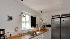 Eine moderne Küche mit weißen Schränken, einem Edelstahl-Kühlschrank, einer Holzarbeitsplatte und Pendelleuchten.