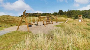 Ein Spielplatz mit Schaukeln und einer Rutsche, umgeben von Gras und Bäumen.