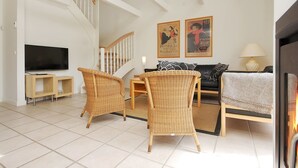 Ein geräumiges Wohnzimmer mit Fernseher, Korbsesseln, einer Couch und einer Treppe.
