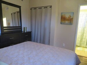 Een slaapkamer met een bed, een kaptafel, een spiegel, een raam met gordijnen en een schilderij aan de muur.